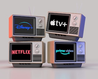 Four old-style television sets are stacked in two rows and each screen displays a different streaming service logo: Disney+, Apple TV+, Netflix, and Prime Video.